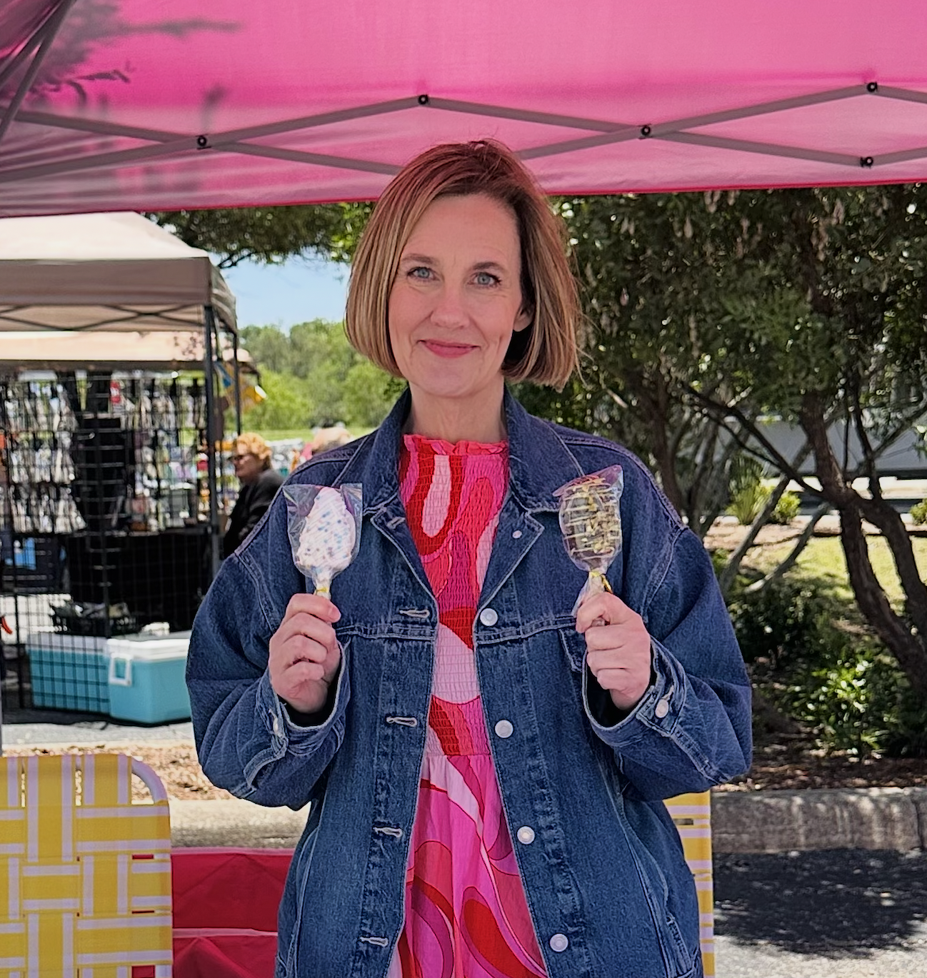 Wendy, owner of Salty Graham Cracker, smiling at her market booth holding two cakesicles